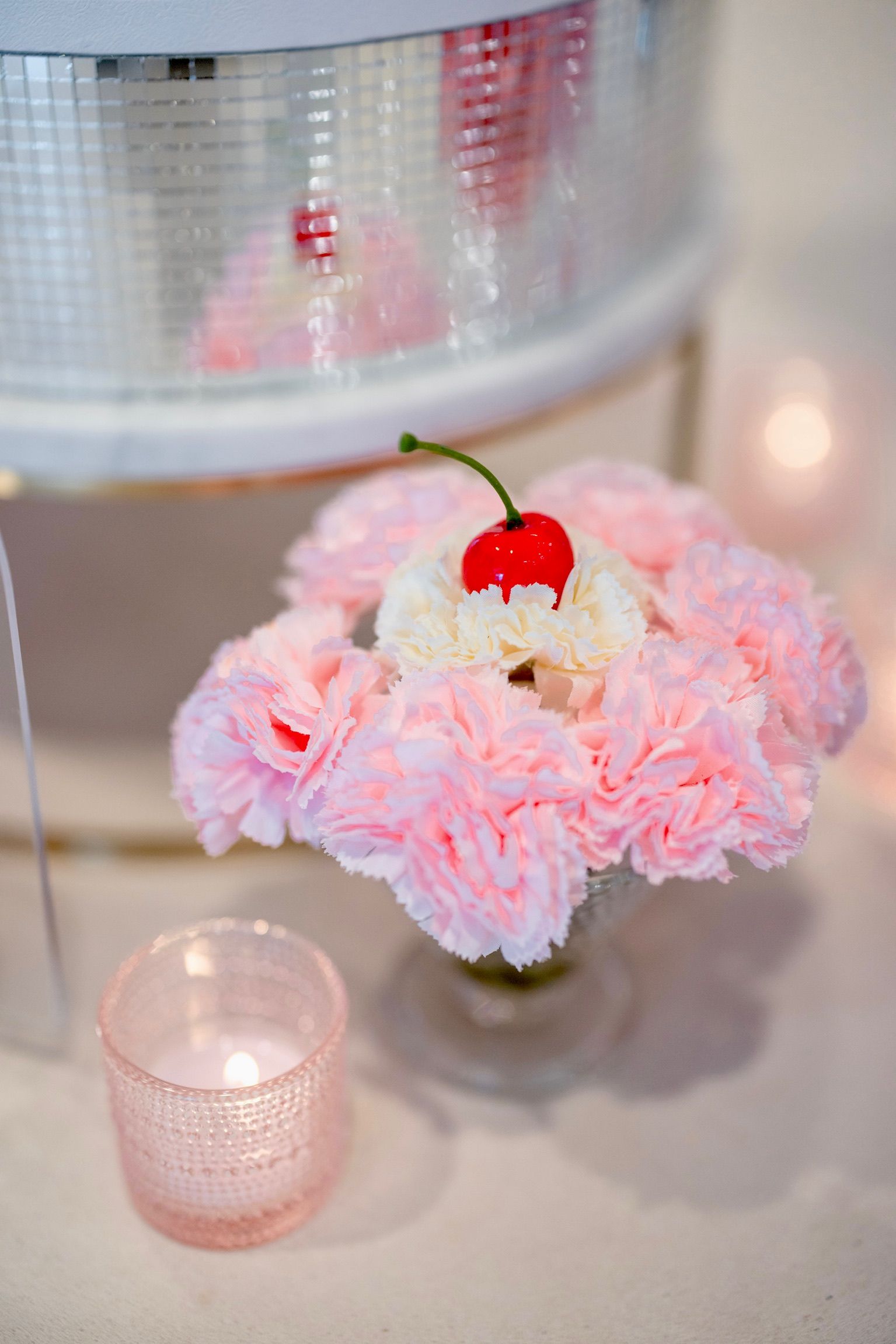 A vase filled with pink flowers and a cherry on top.