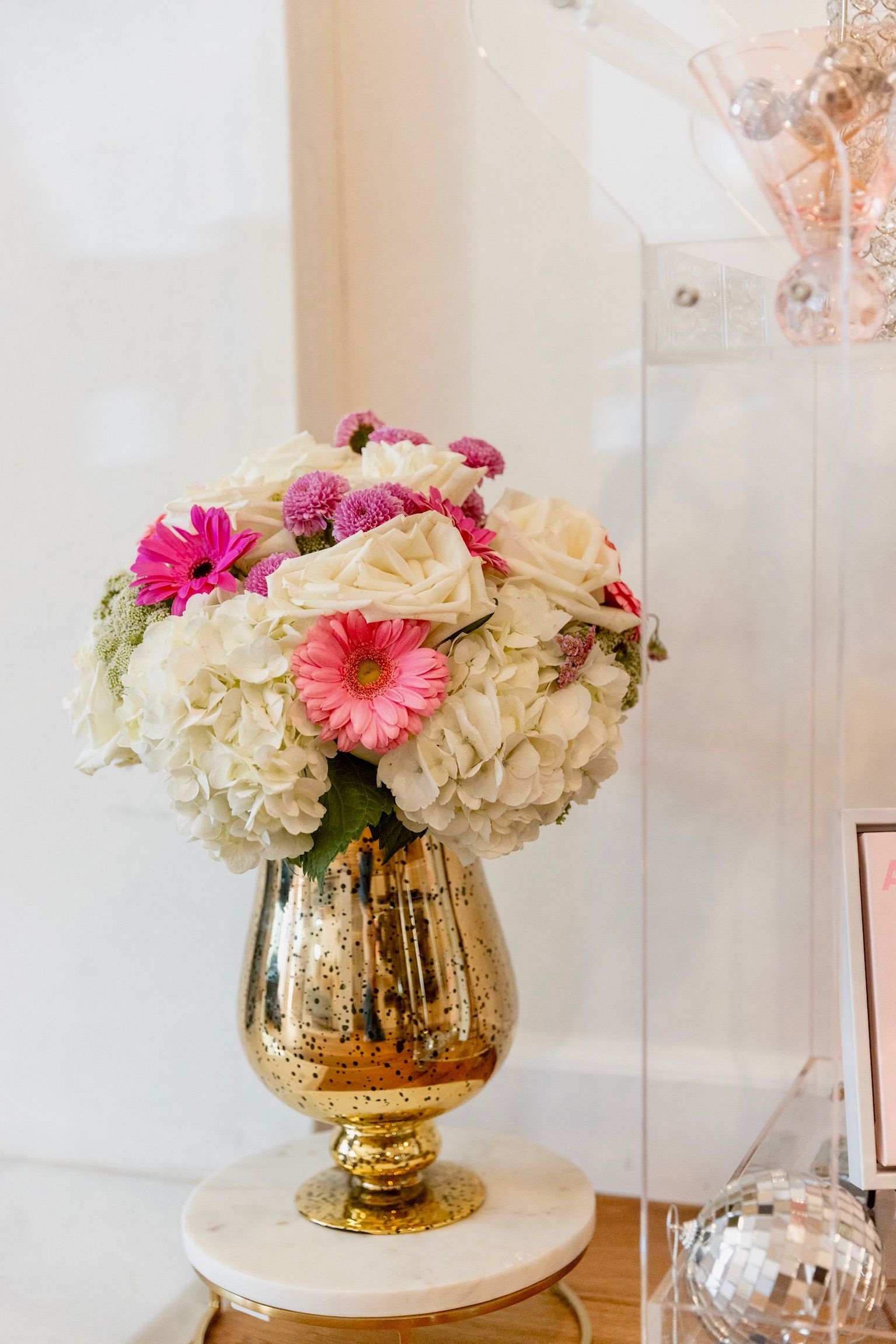 A gold vase filled with pink and white flowers is sitting on a table.
