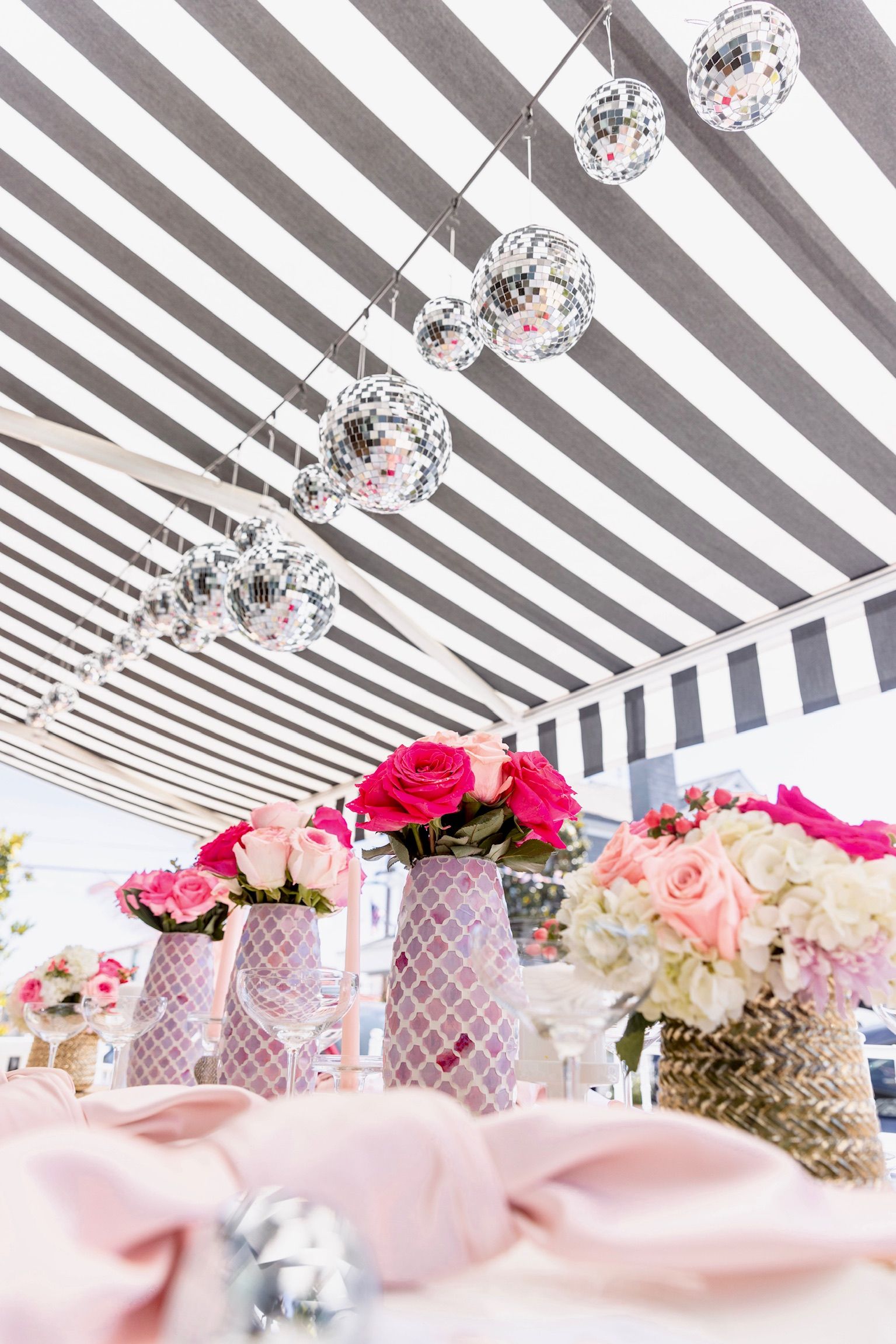 A table with flowers in vases under a striped canopy.