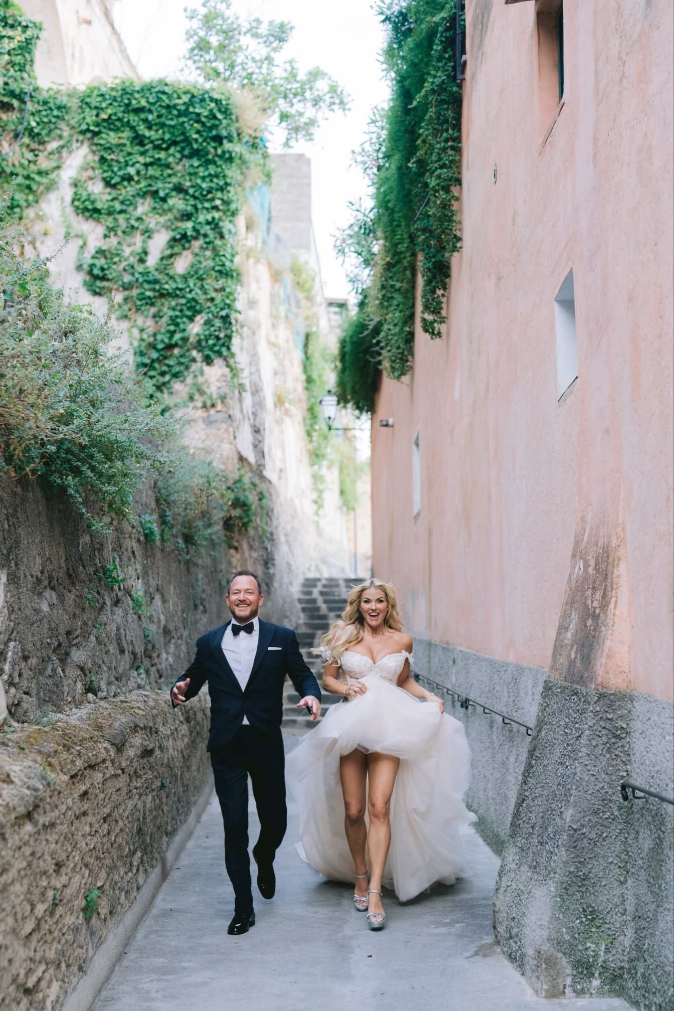 A bride and groom are running down a narrow street.