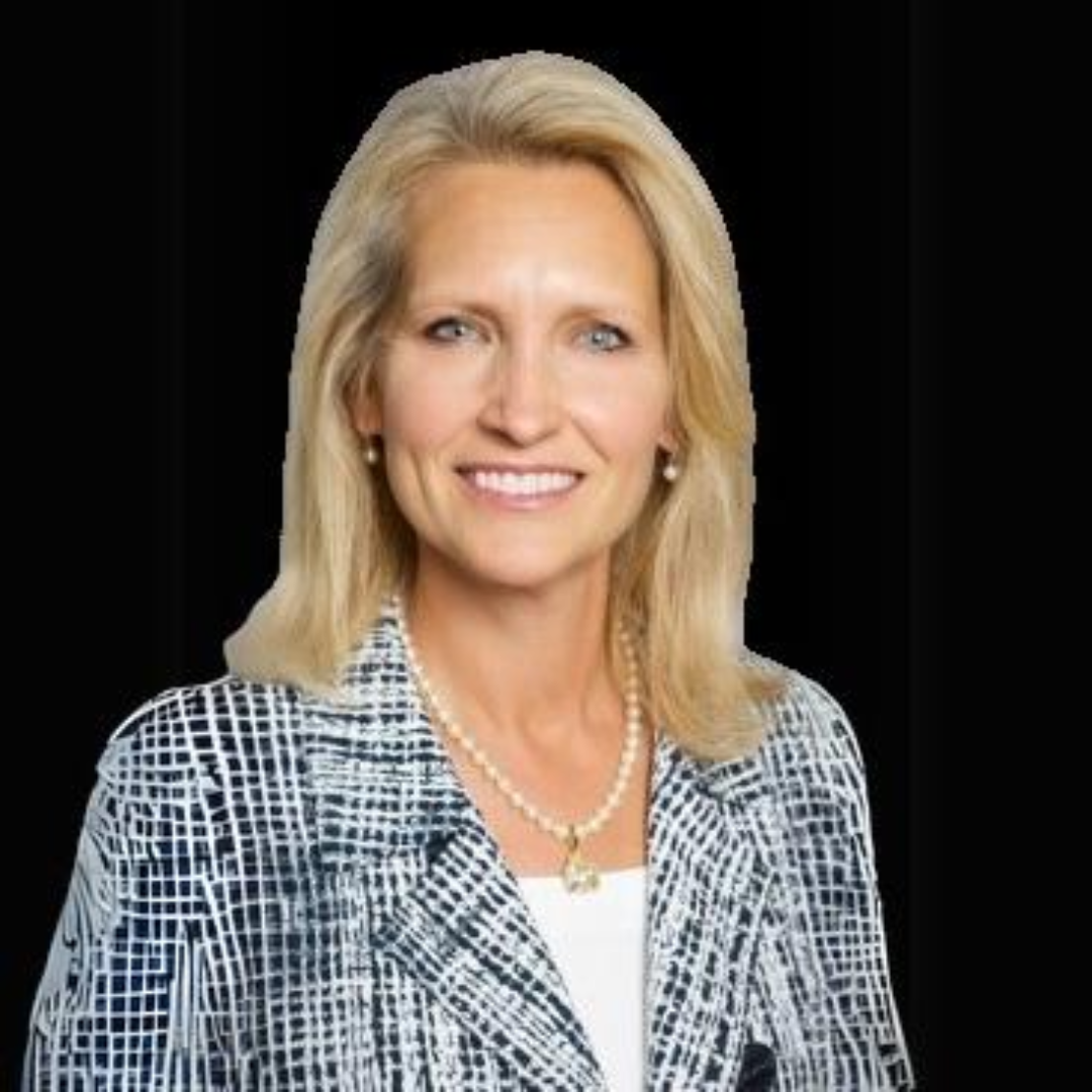 A woman wearing a plaid jacket and a pearl necklace is smiling for the camera.