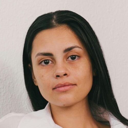 Portrait of a woman with straight dark hair, wearing a white shirt, against a plain light background