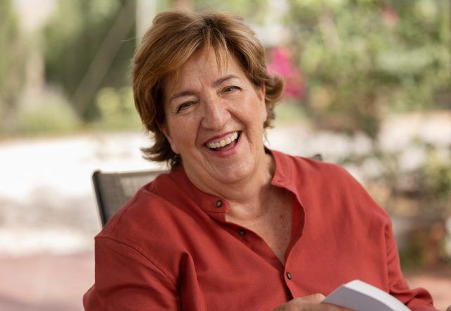 Smiling woman in a red shirt seated outdoors with a blurred garden background