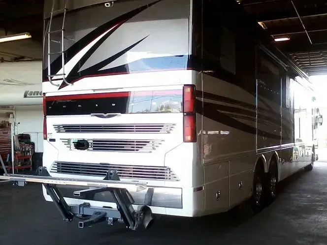 Rear view of a white and brown RV with a tow hitch, parked inside a garage.