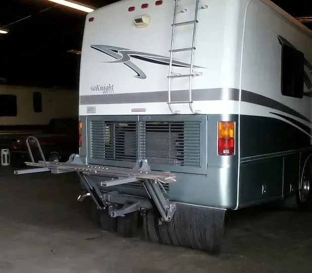 Rear of a motorhome with a hitch and brush guards, in a garage.