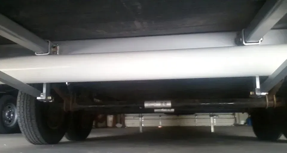 Undercarriage of a trailer. Black tires, a steel axle, and a white tank are visible.