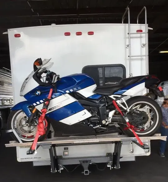 Blue and white motorcycle strapped to a lift on the back of a white RV.