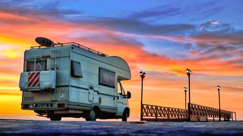 RV parked on a pier at sunset; orange and blue sky.