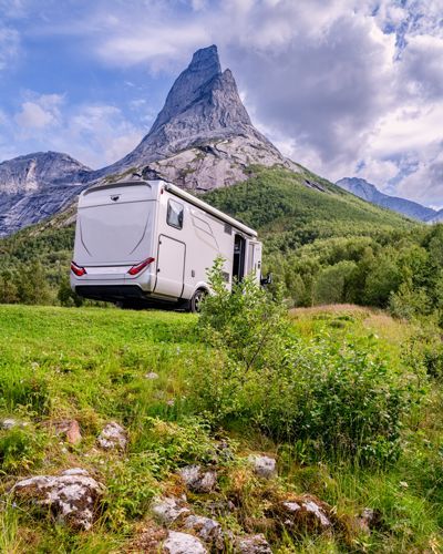 RV parked on a grassy hill with a mountain peak in the background.