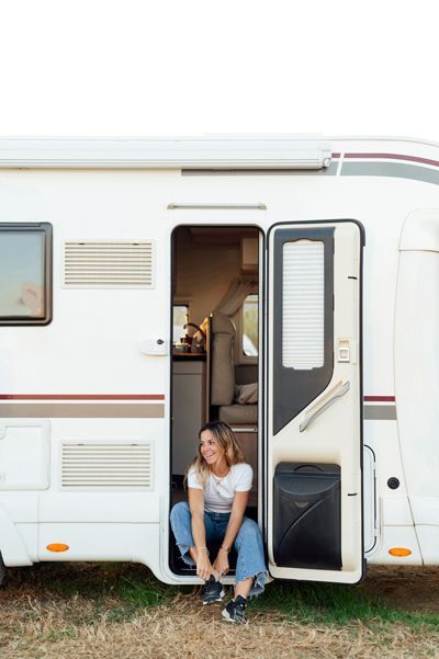 Woman in blue jeans and white shirt sits in RV doorway, smiling.