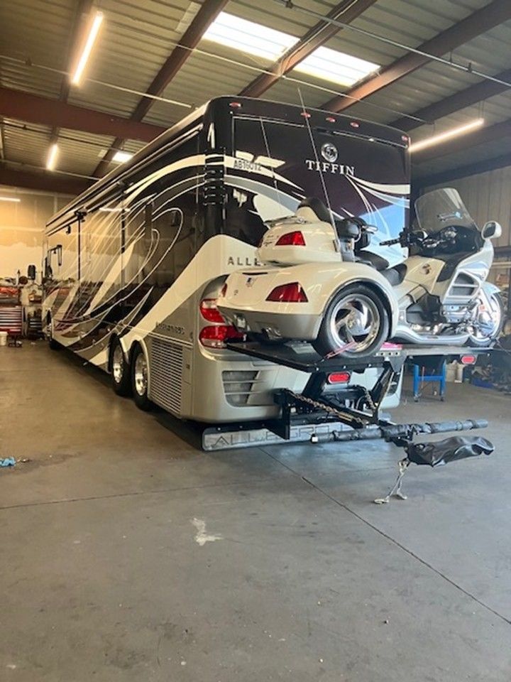 Large RV with car and motorcycle hitched, parked in a garage. Beige, black, and white.