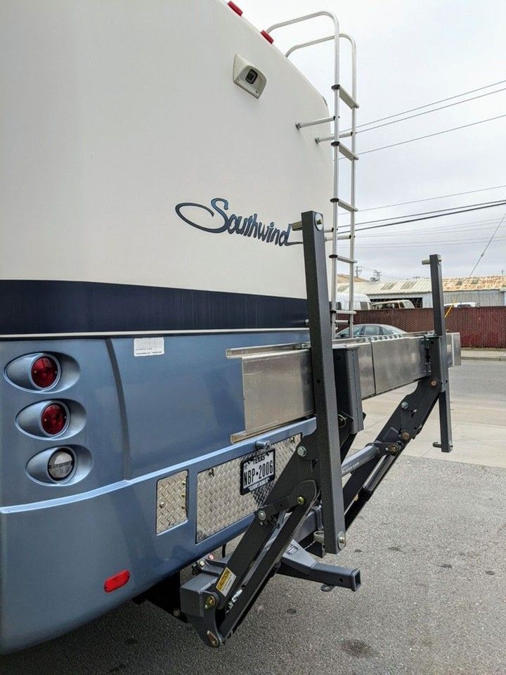 Rear of a blue and white RV, with a ladder and attached cargo carrier.