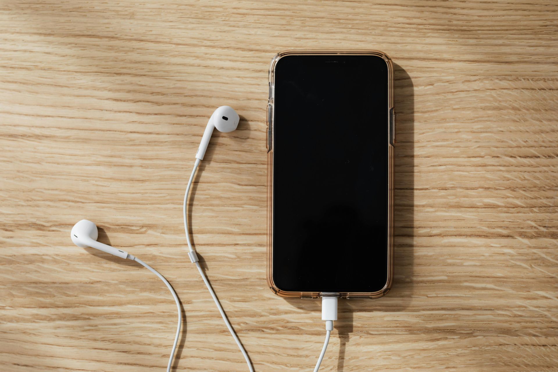 A cell phone with headphones attached to it is sitting on a wooden table.
