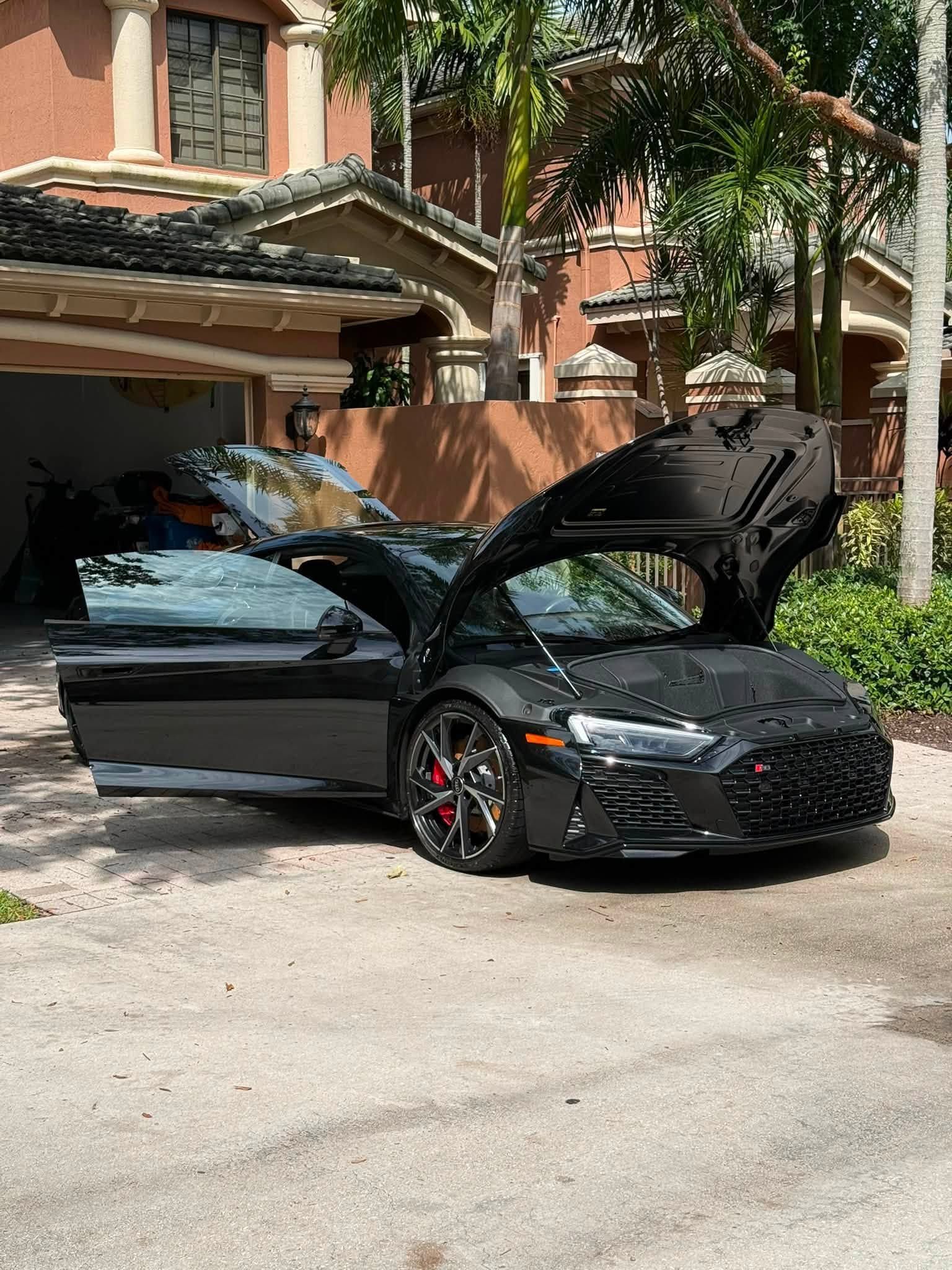 Black sports car with doors and hood open parked outside a brick building