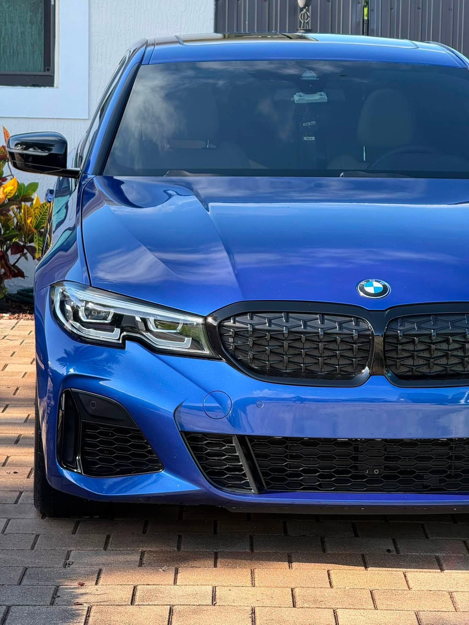 Blue BMW sedan parked on a brick driveway in front of a house.