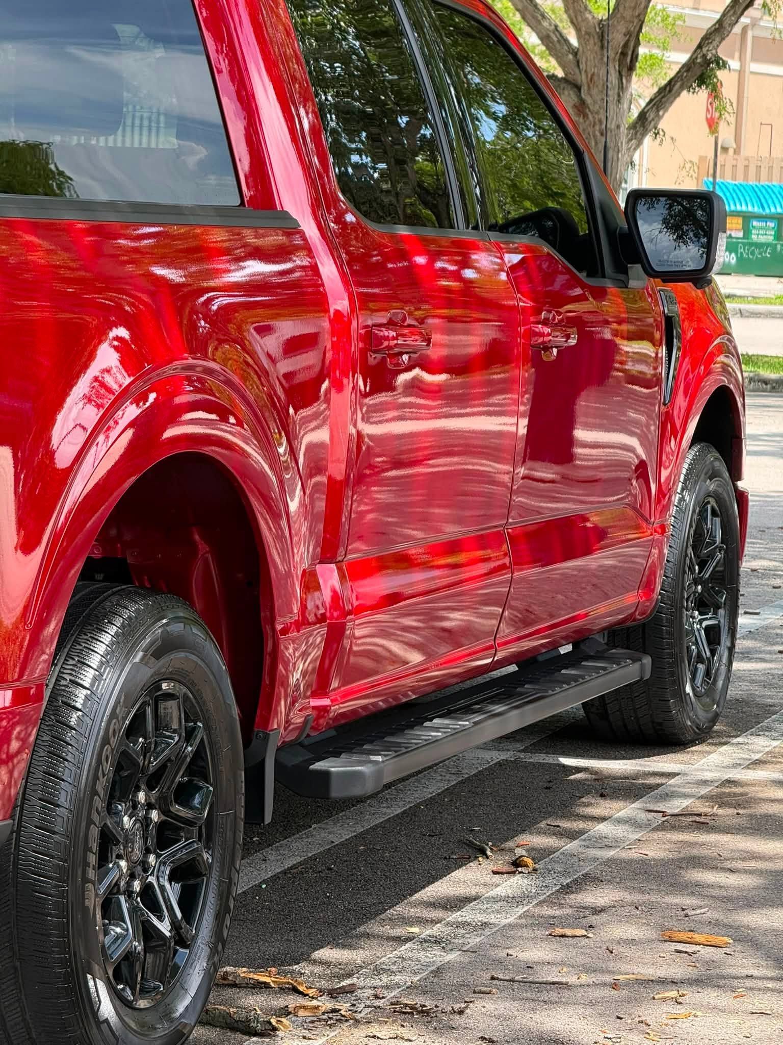 Red pickup truck parked on a driveway beside a house, with glossy paint and black wheels