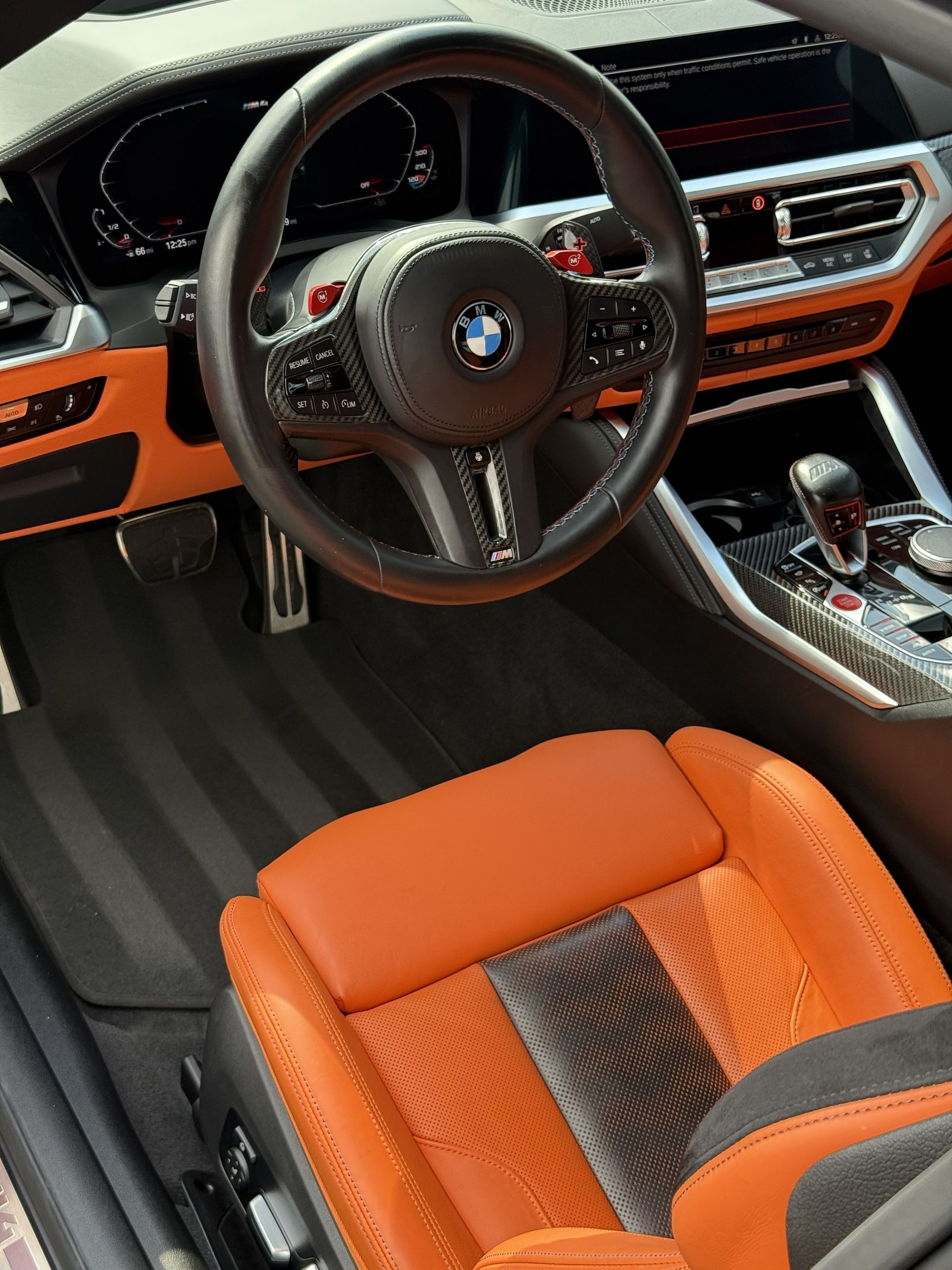 The interior of a BMW with orange leather bucket seats, a black leather steering wheel, and a digital dashboard display.