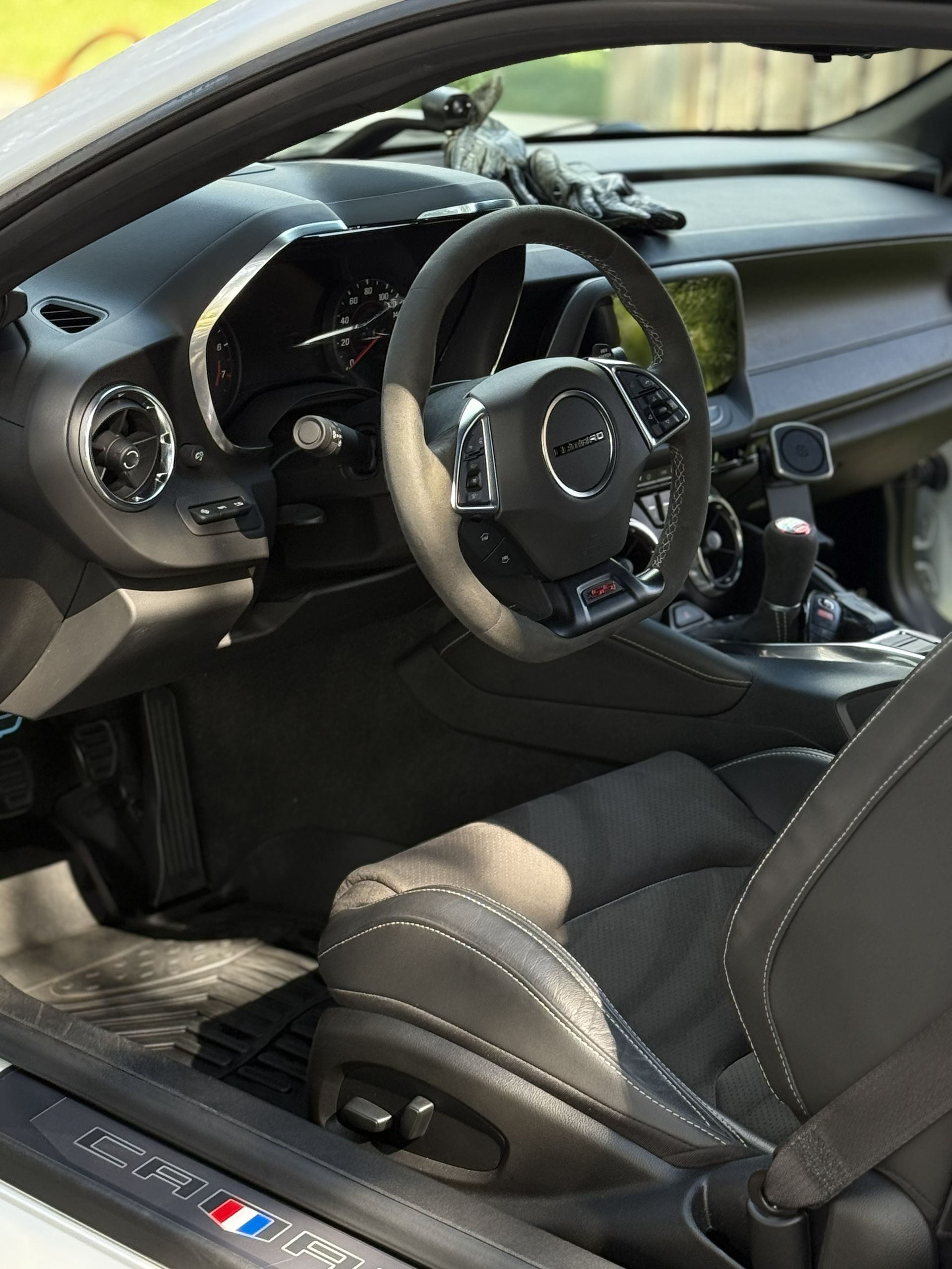 The interior of a Chevrolet Camaro with black seats, a leather steering wheel, and a French flag emblem on the door sill.