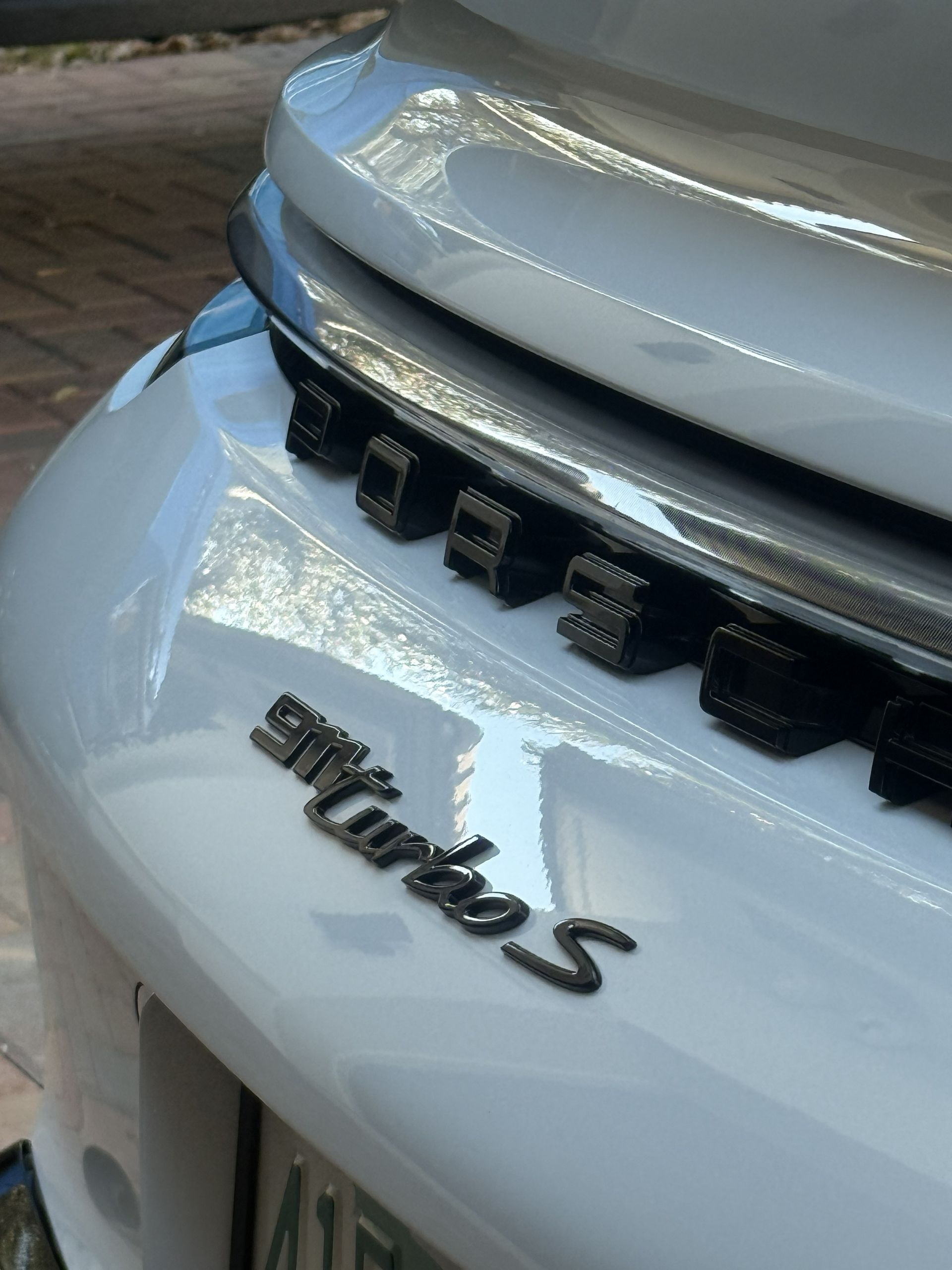 A close-up of a white Porsche 911 Turbo S rear badge and engine grille detail.
