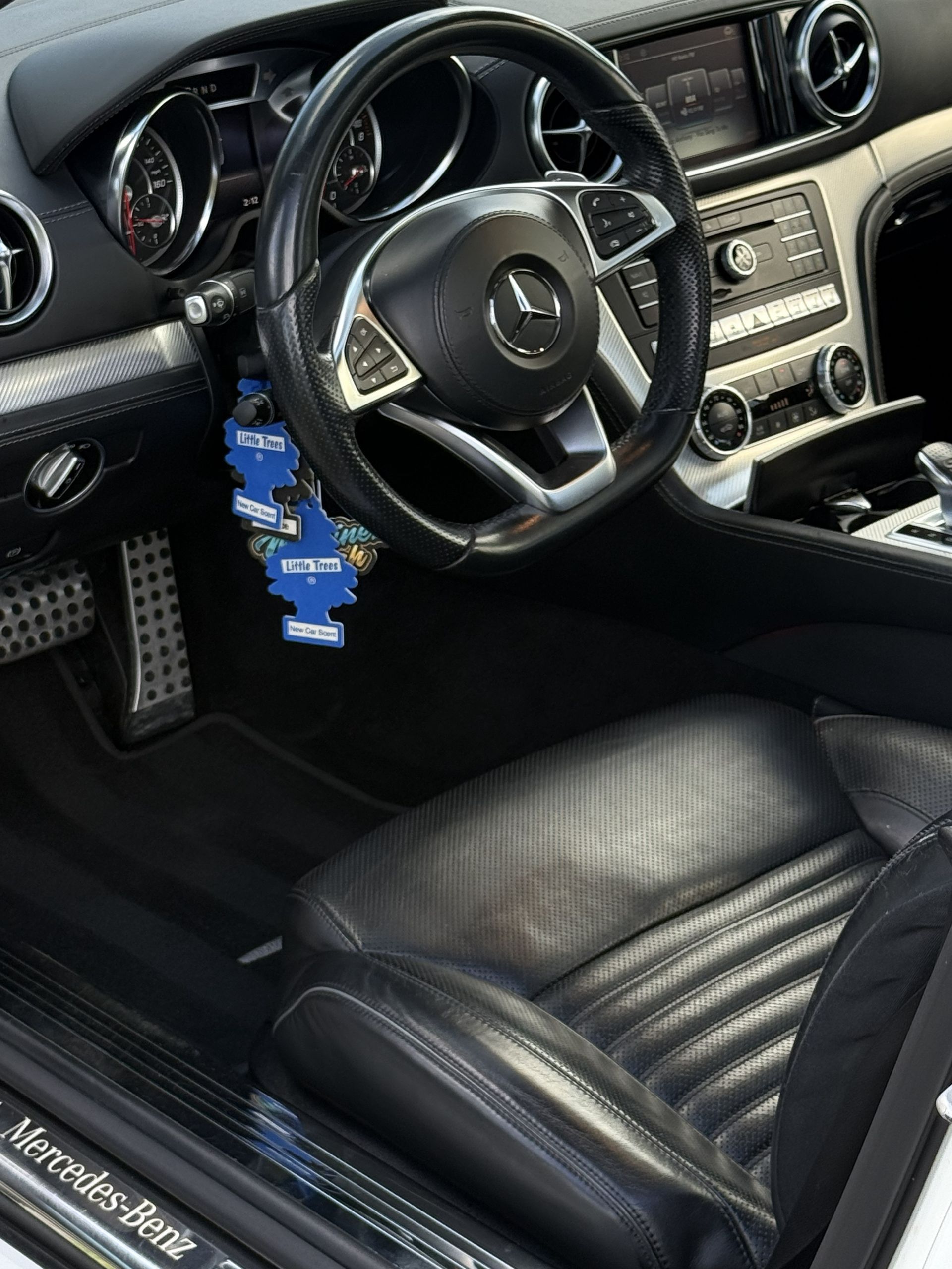 Interior of a Mercedes-Benz featuring a black leather seat, a sports steering wheel, and a blue air freshener hanging.