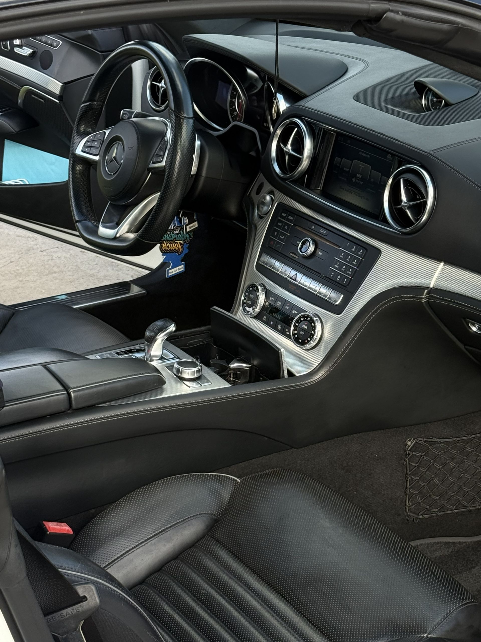 A close-up interior view of a luxury Mercedes-Benz vehicle with black leather seats, steering wheel, and silver trim.