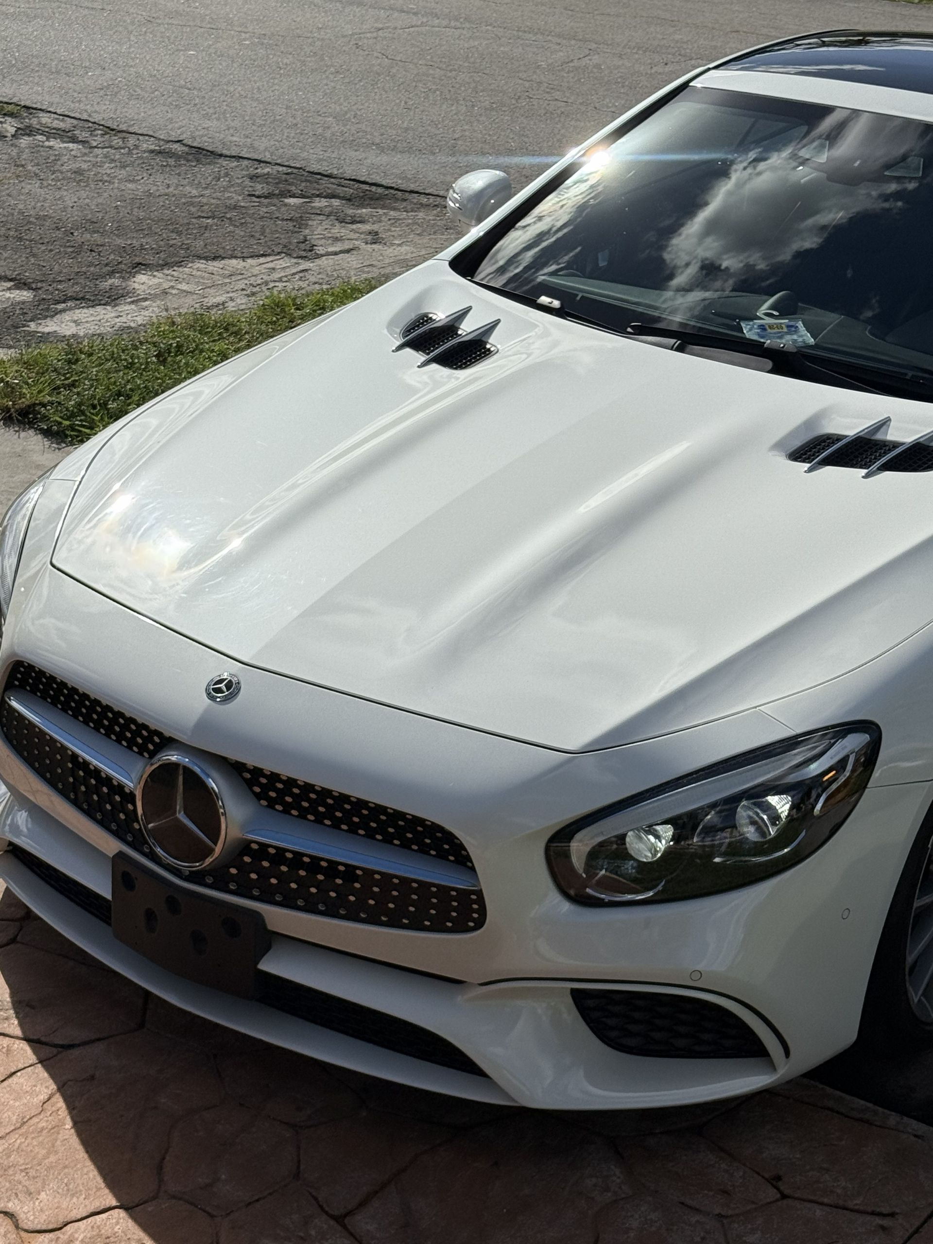 A white Mercedes-Benz SL-Class convertible parked on a paved driveway.