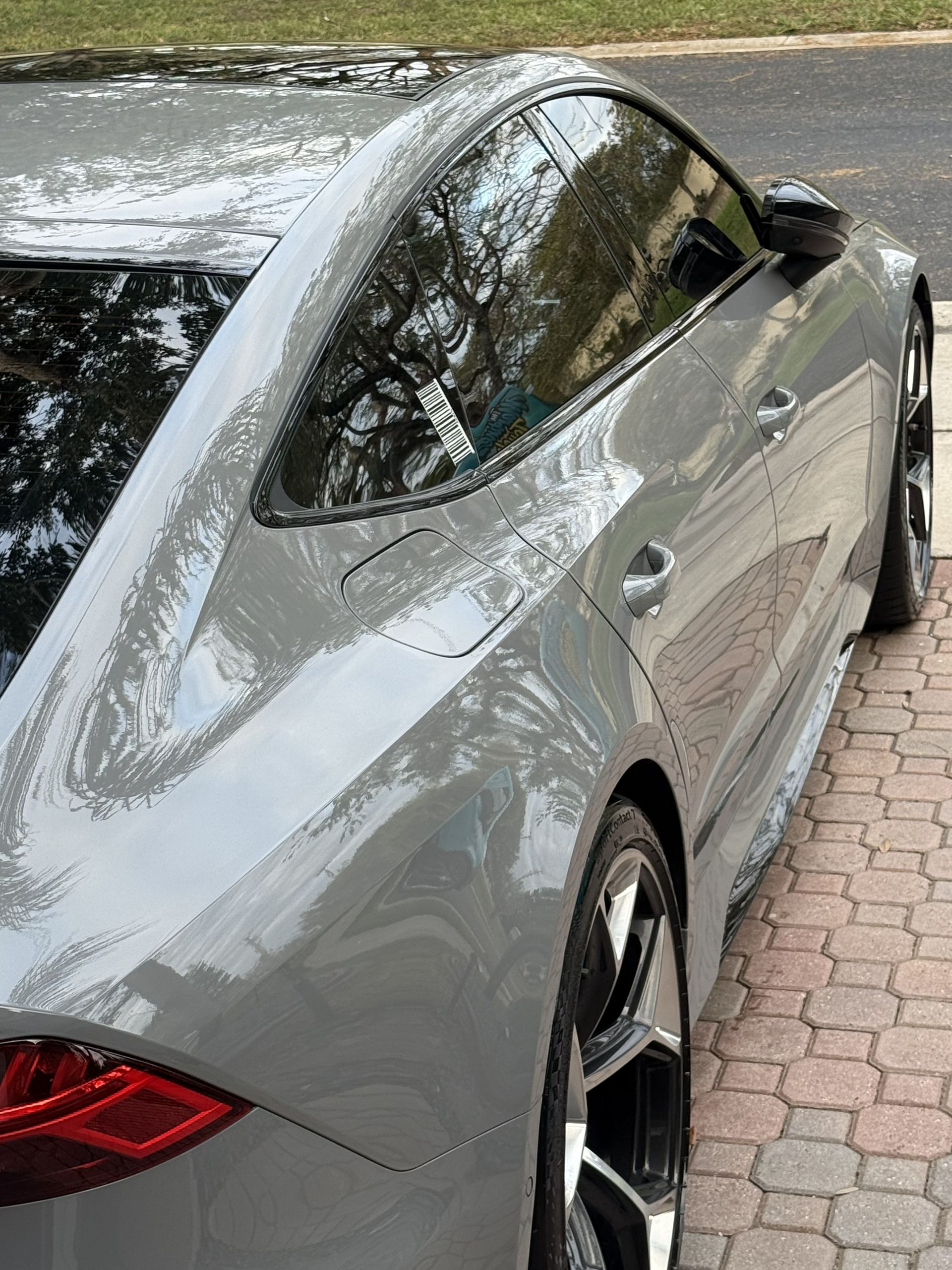 A sleek, grey sedan parked on a brick driveway, viewed from the rear quarter angle to highlight its body lines and wheels.