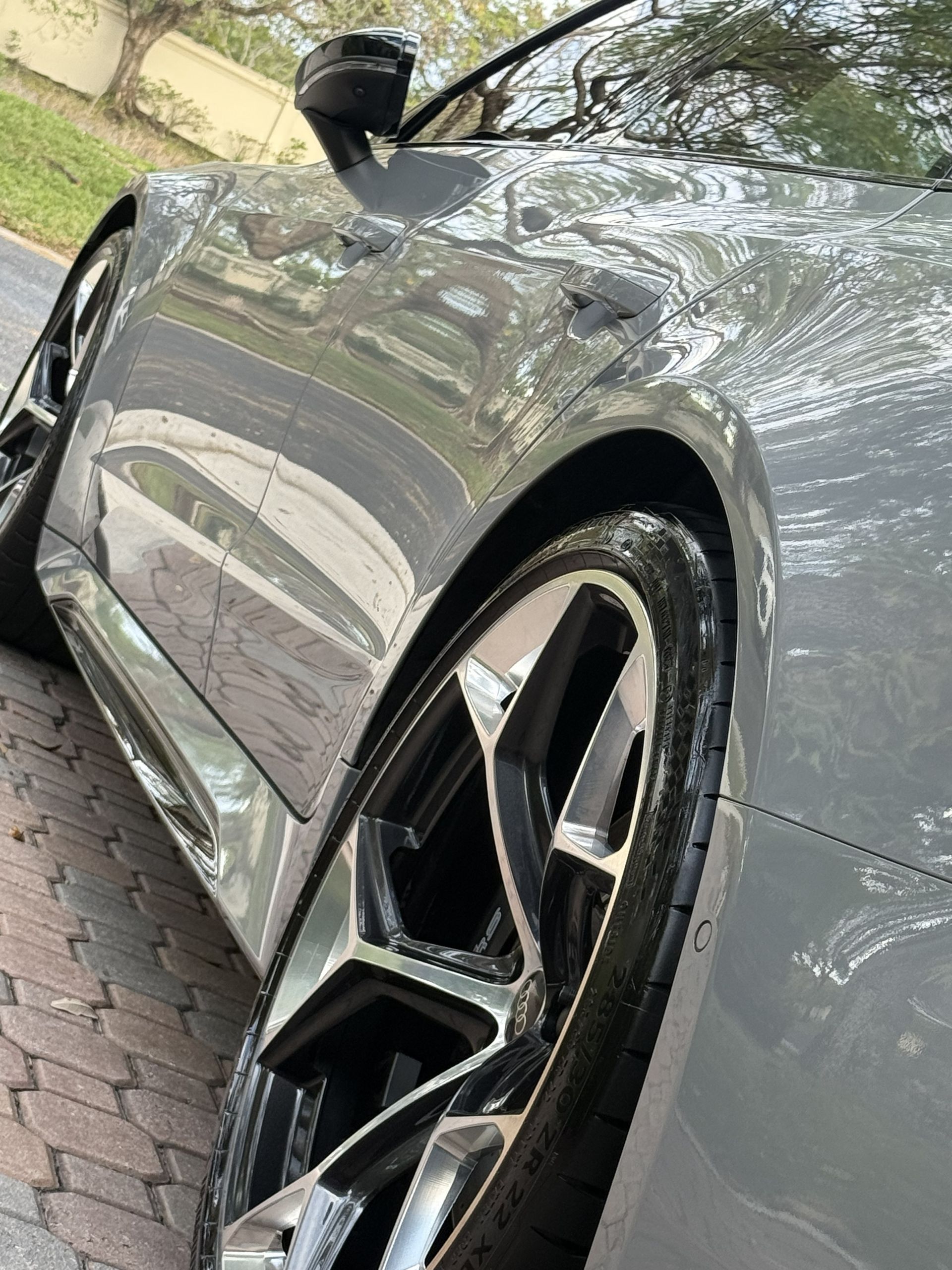 A close-up, angled view of the side and custom black and silver alloy wheel of a sleek, grey sports car.