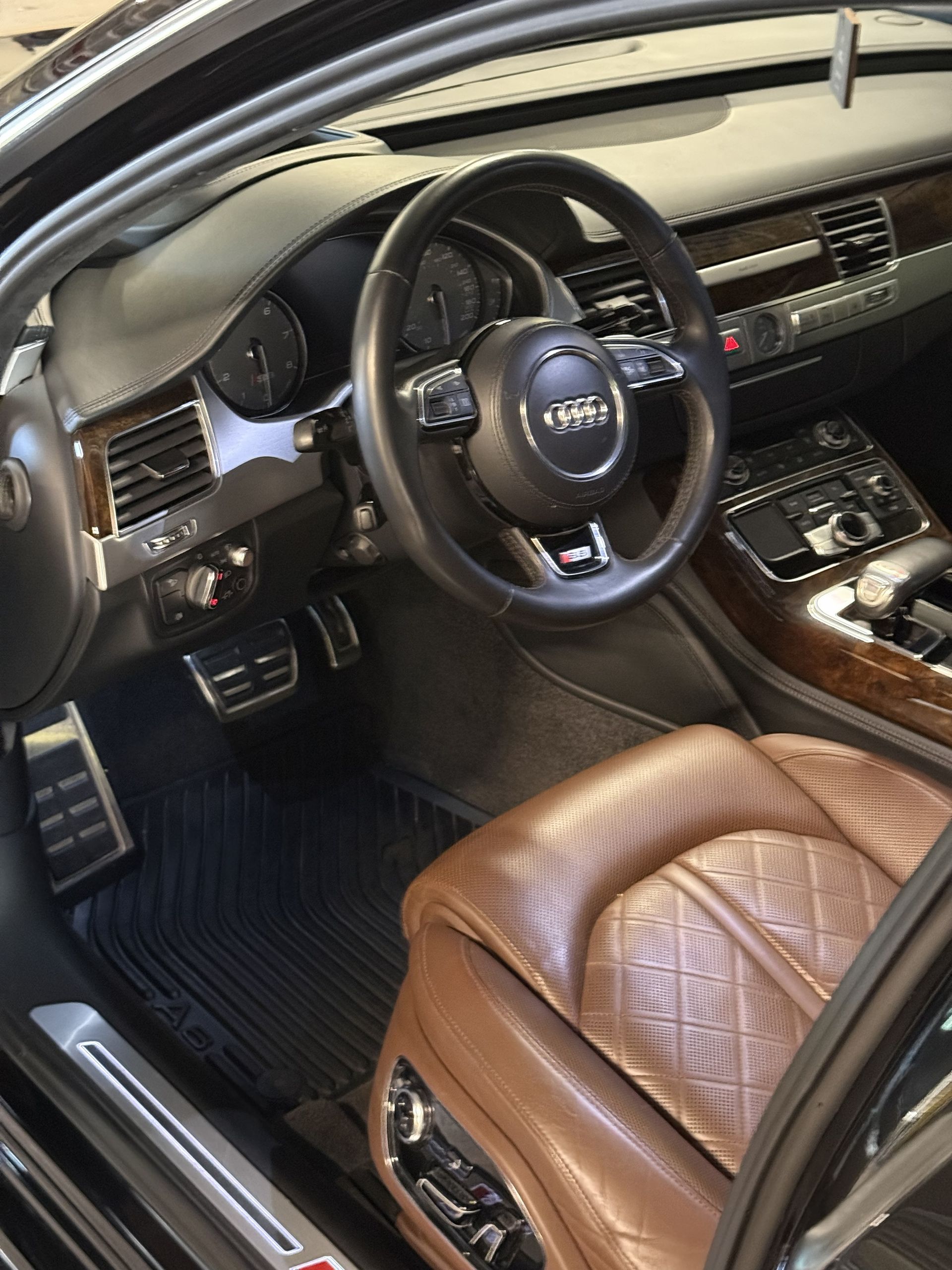 Luxury car interior featuring brown diamond-stitched leather seats, a dark dashboard, and an Audi steering wheel.