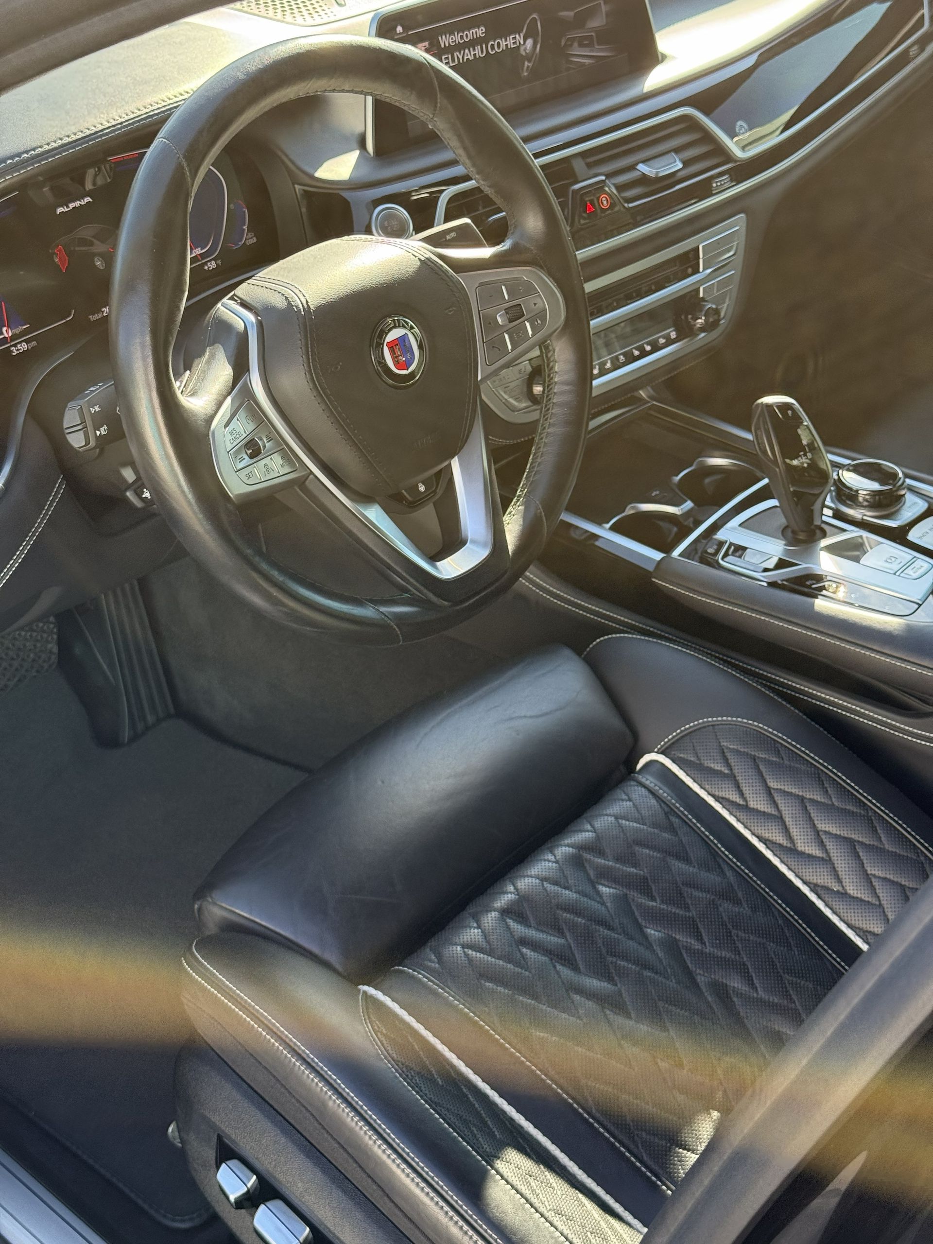 The interior of a black luxury car with leather seats, an Alpina steering wheel, and a center console gear shifter.