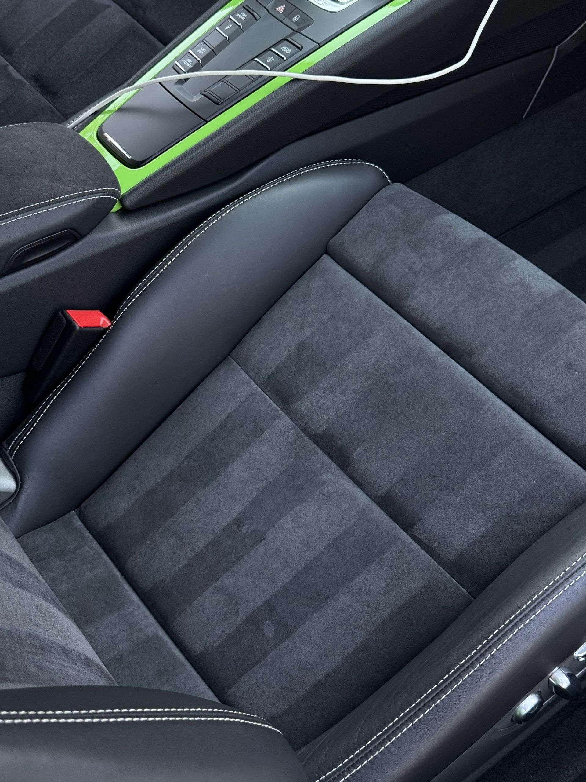 A car seat upholstered in gray suede and black leather with white contrast stitching, next to a lime green console.