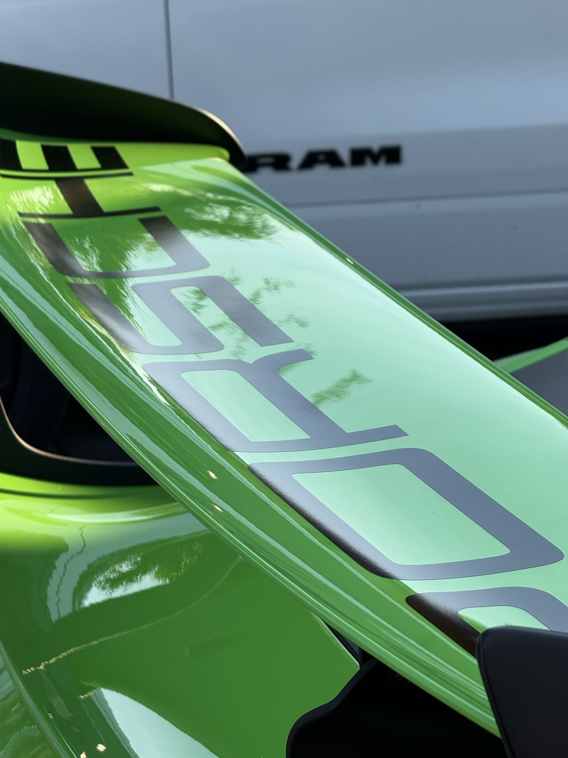 Close-up of a vibrant green Porsche sports car rear spoiler featuring the brand name in large, dark block lettering.