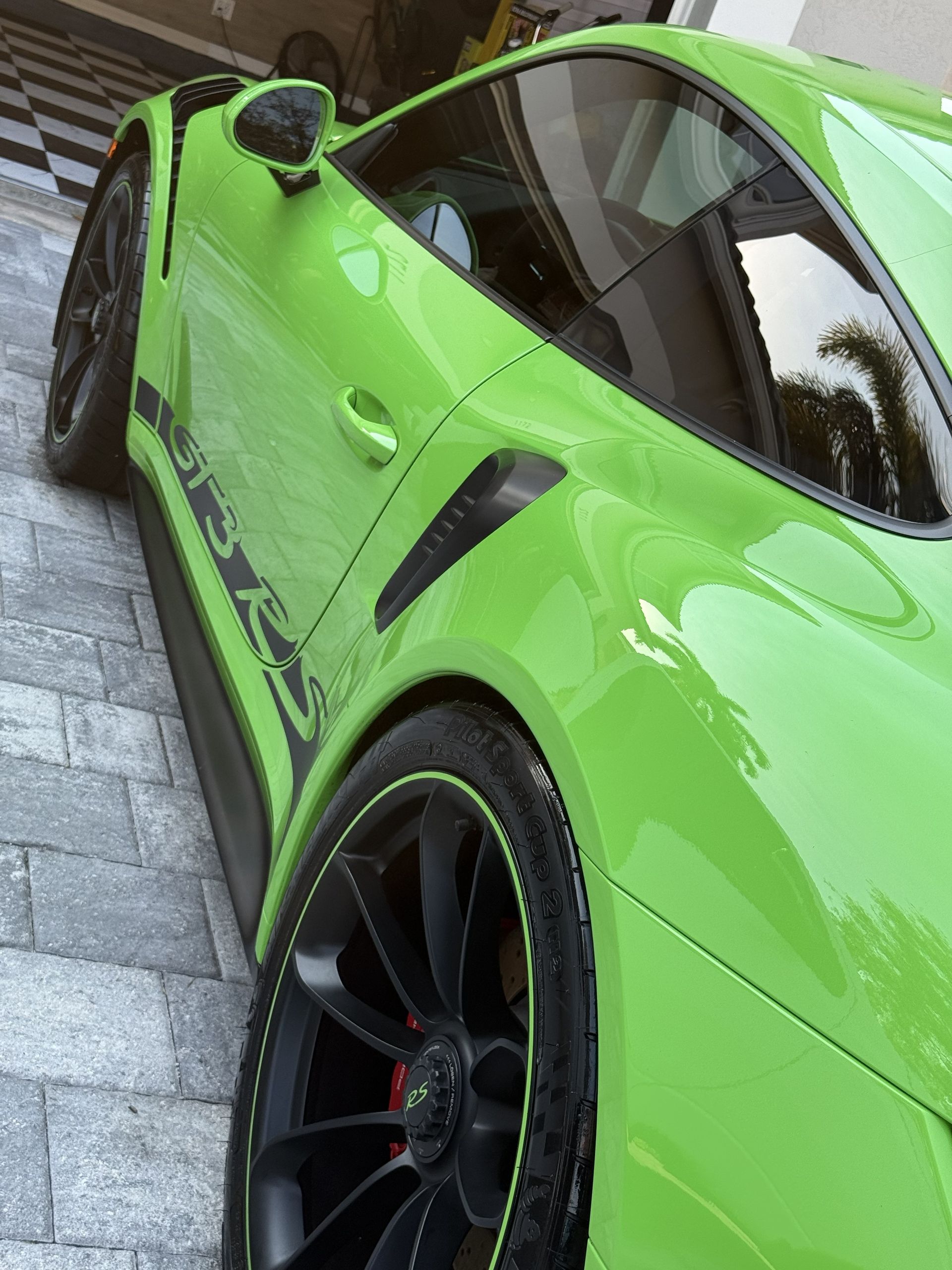 Side profile of a bright green Porsche 911 GT3 RS parked on a paved driveway.