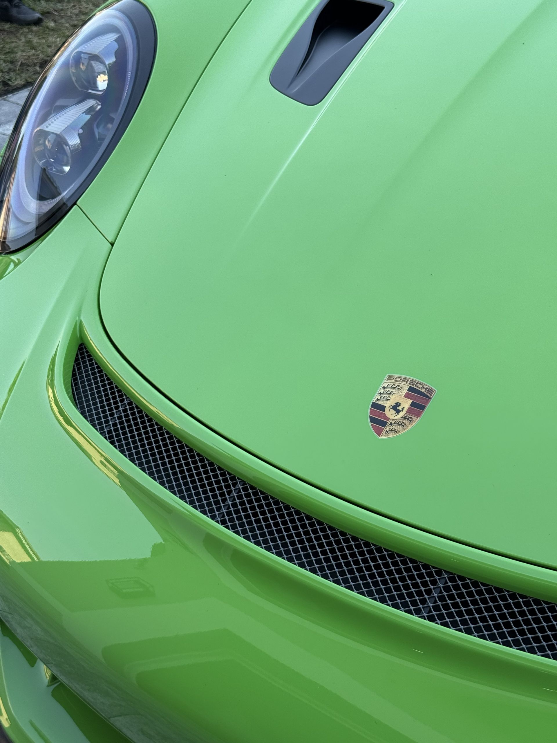Close-up of a bright green Porsche hood, featuring its emblem and a black mesh air intake.