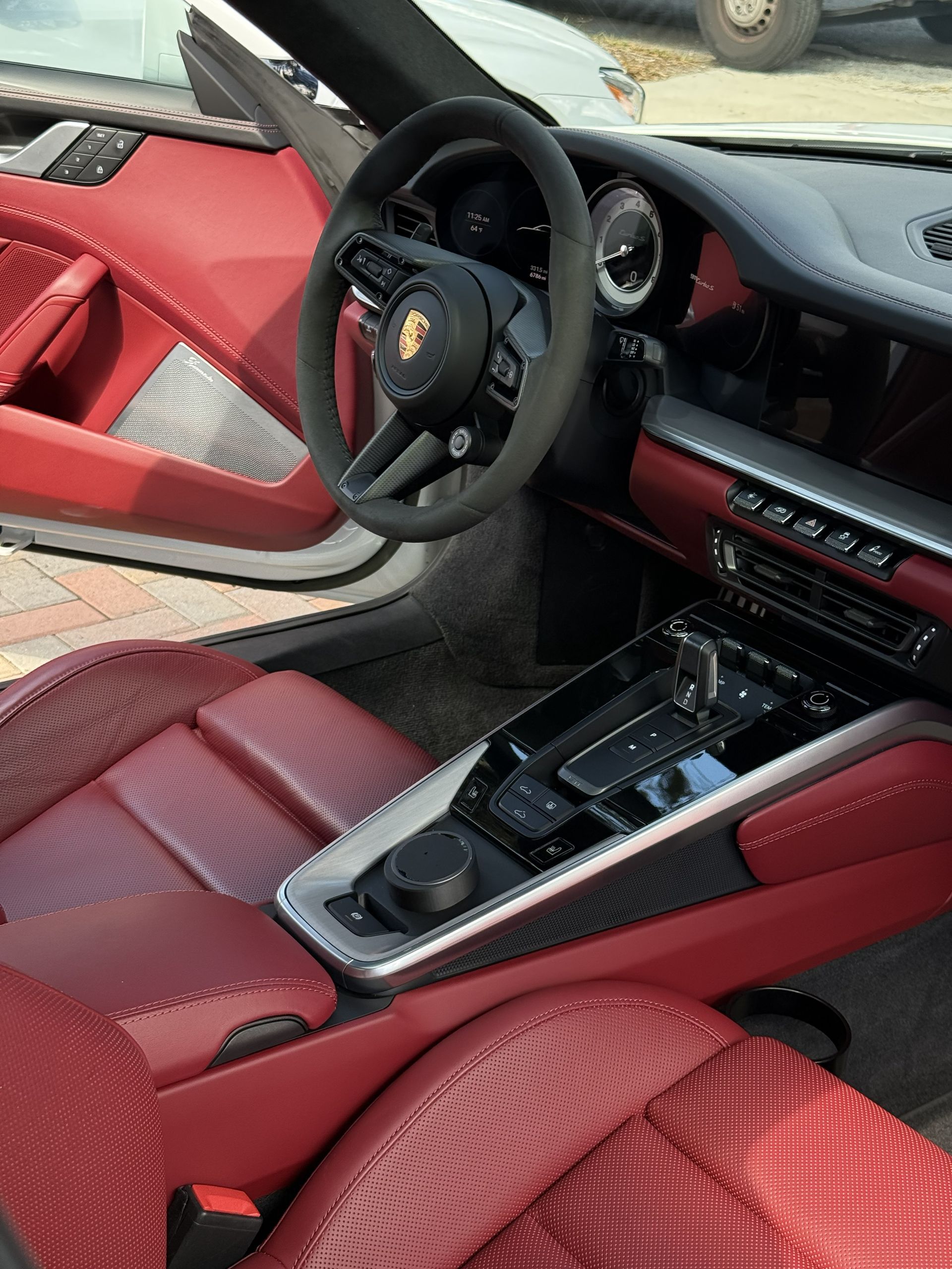 The interior of a Porsche with red leather seats, a dark suede steering wheel, and a carbon fiber center console.