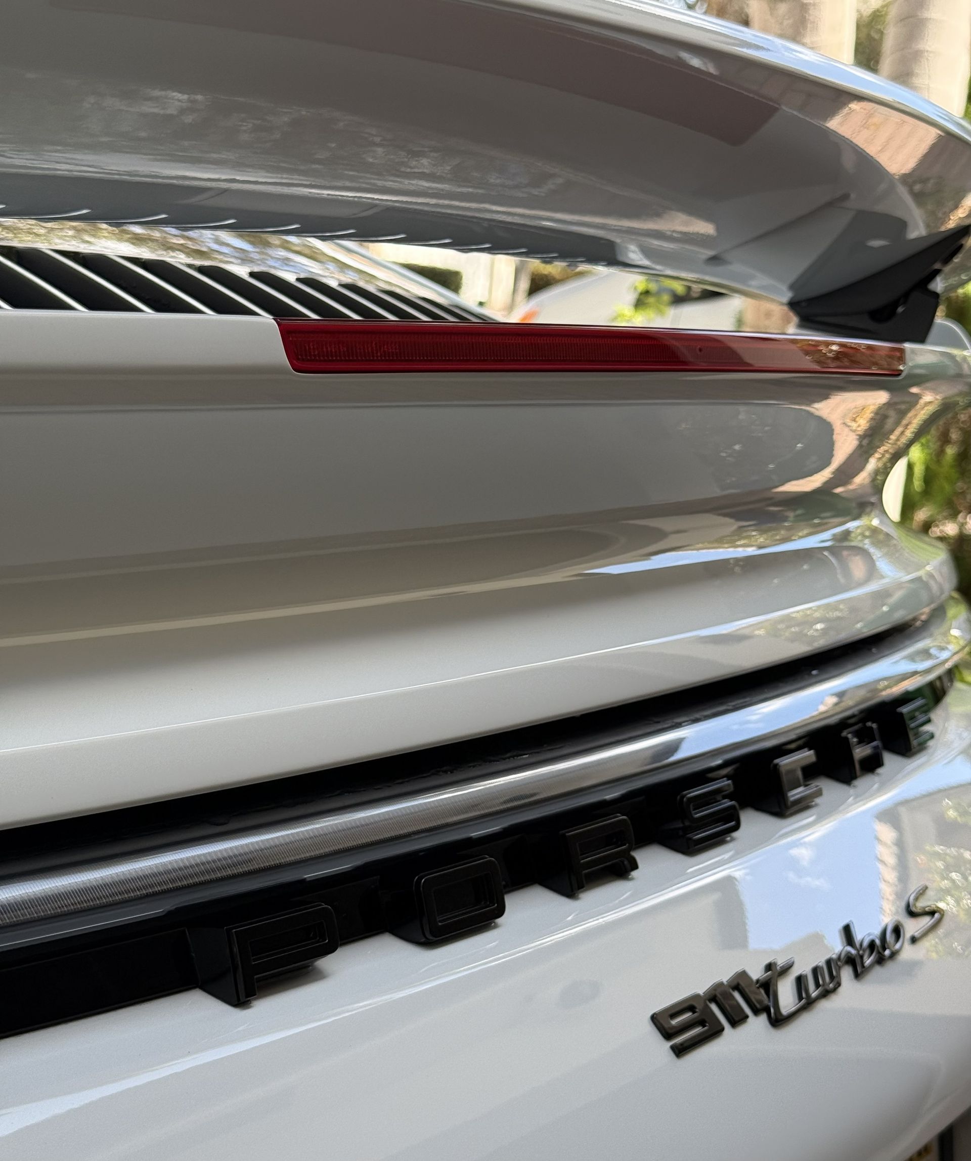 Close-up of the rear deck lid and spoiler of a white Porsche 911 Turbo S with black lettering.