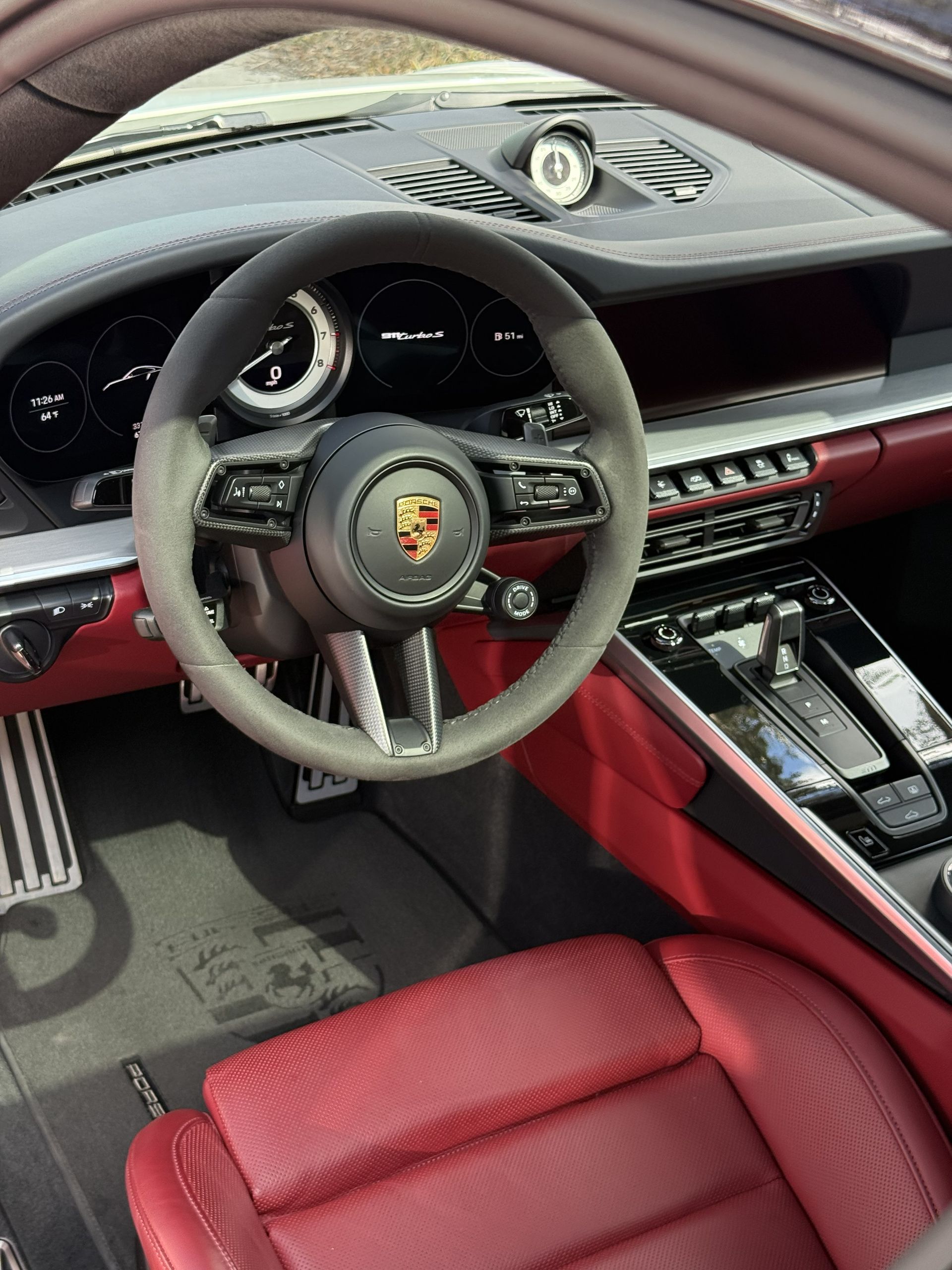 Driver's view of a luxury Porsche car interior with a black steering wheel and red leather seats.