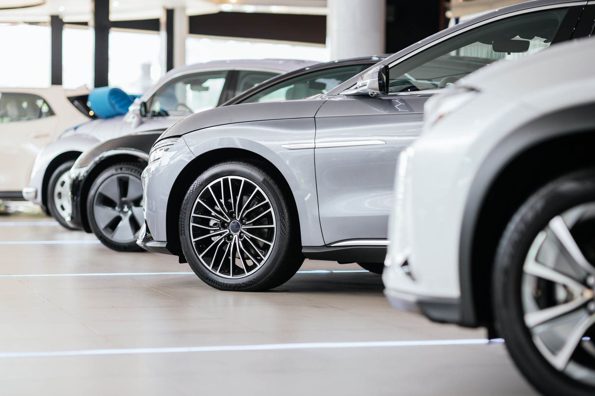 Row of parked cars in a bright indoor showroom, including a silver car in the foreground.