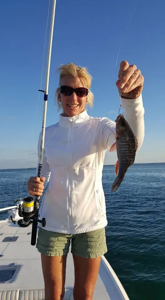 A woman is holding a fish and a fishing rod on a boat.