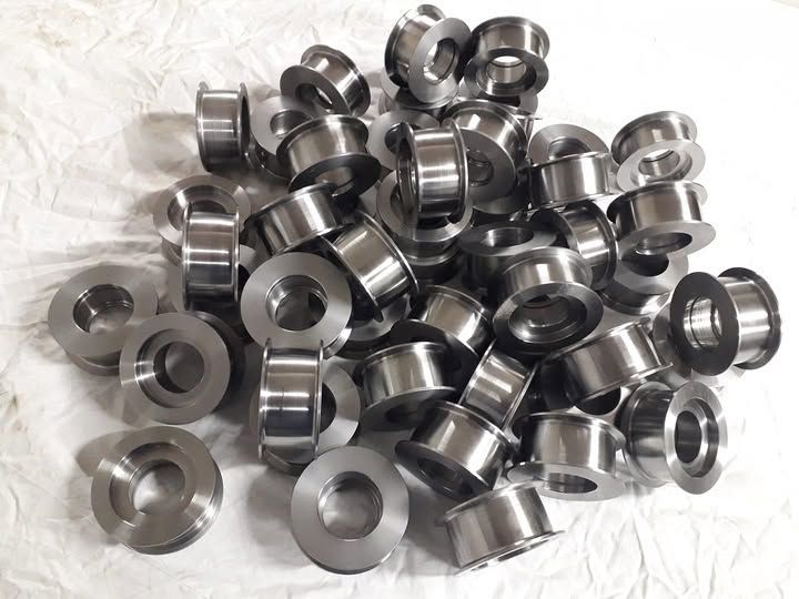 Un mucchio di parti cilindriche di metallo lucido con un foro centrale, su una superficie bianca.