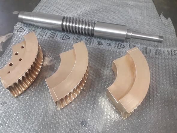 Ingranaggi metallici e un albero filettato su una superficie grigia, probabilmente parti di macchine industriali.