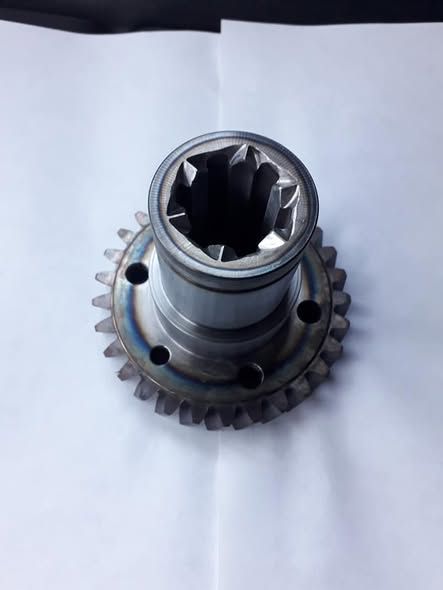 Ingranaggio metallico con denti e foro scanalato centrale, appoggiato su una superficie bianca.