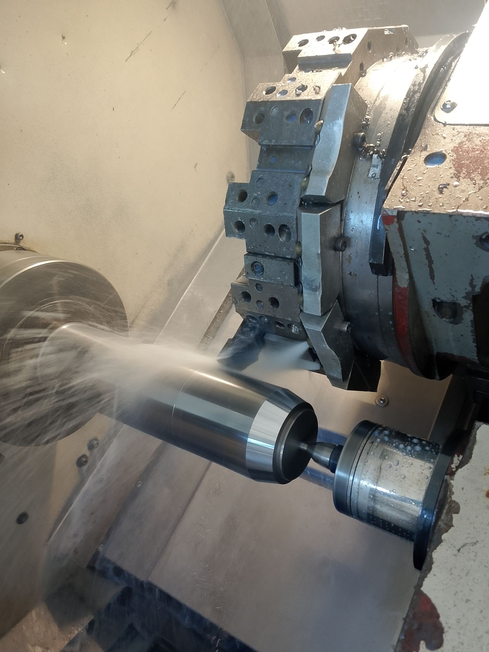 Macchina CNC che gira un cilindro di metallo, spruzzando refrigerante.