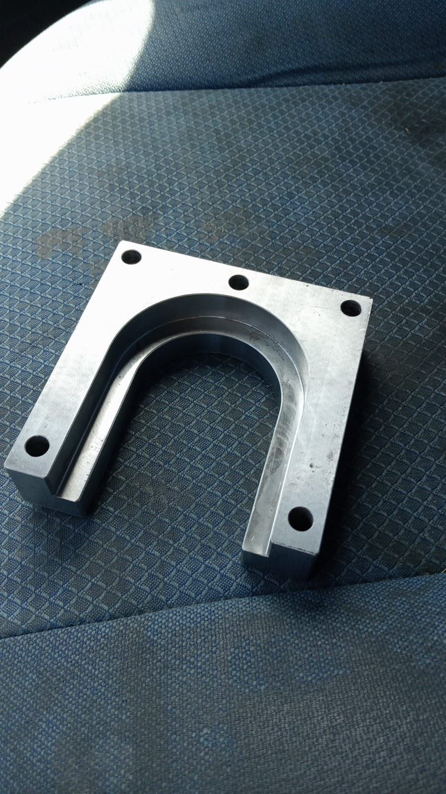 Staffa a U in metallo argentato con quattro fori di montaggio, appoggiata su una superficie decorata con motivi blu.