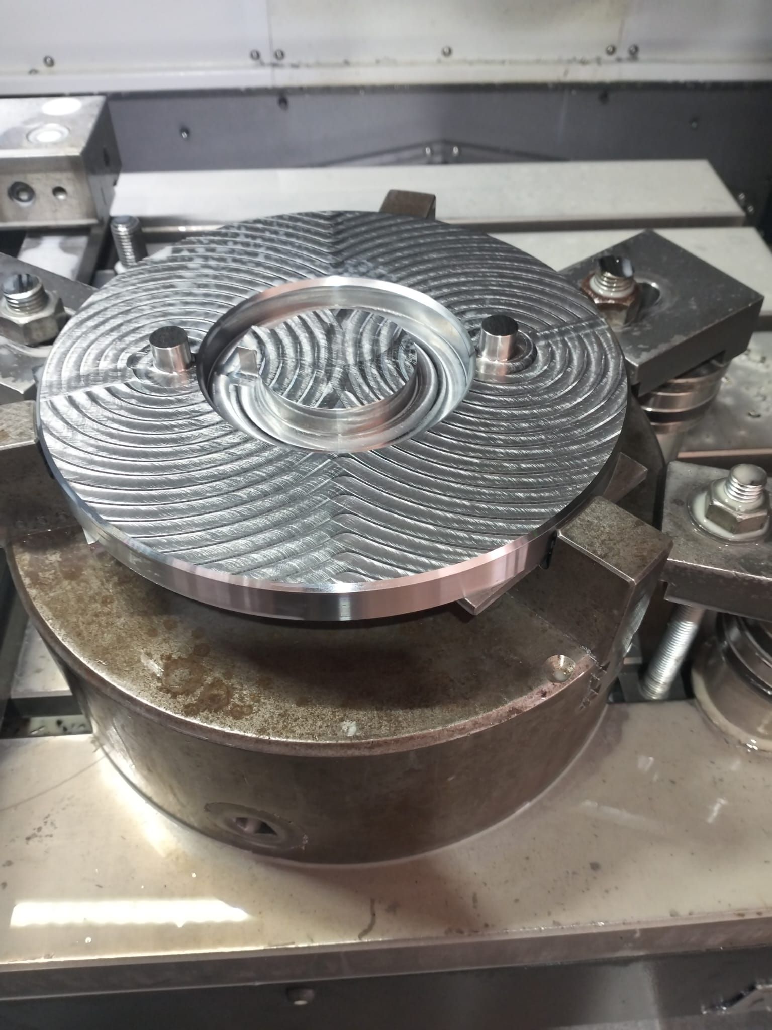 Una piastra metallica lavorata con scanalature a spirale è posizionata su un mandrino della macchina.