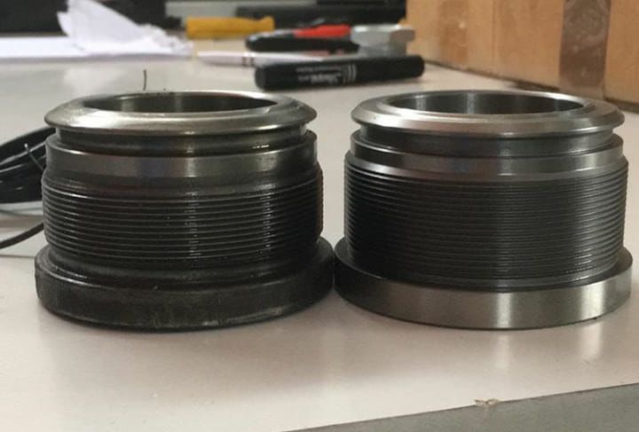 Due parti metalliche cilindriche con estremità filettate, posizionate una accanto all'altra su una superficie bianca.