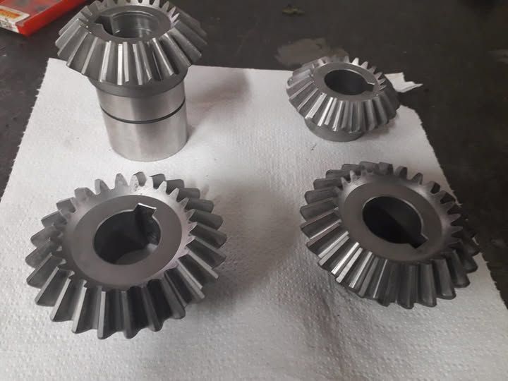 Quattro ingranaggi conici in metallo e un mozzo, appoggiati su un tovagliolo di carta bianco.