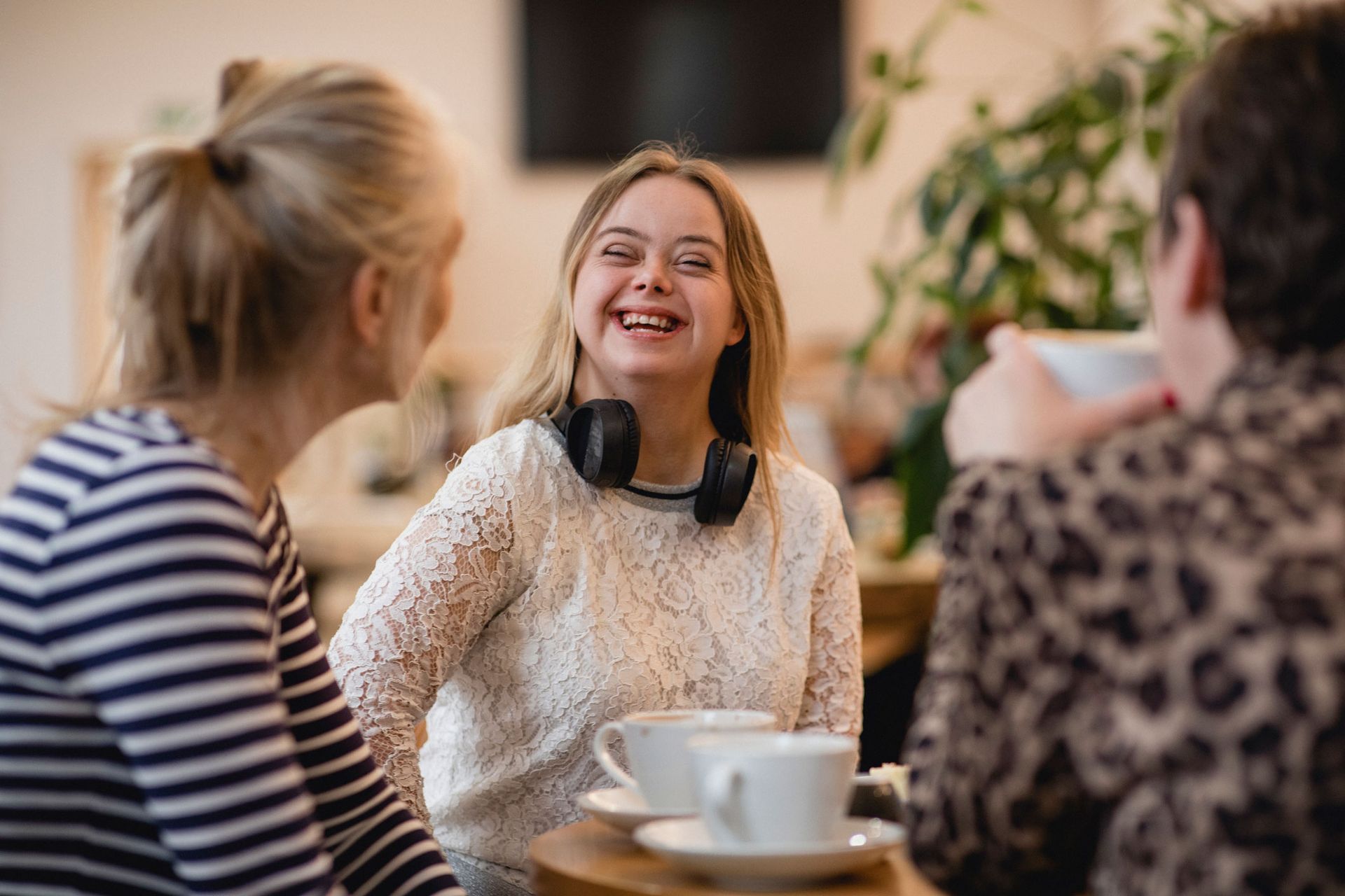 Three people at a cafe; woman with Down syndrome smiles; coffee cups on the table.