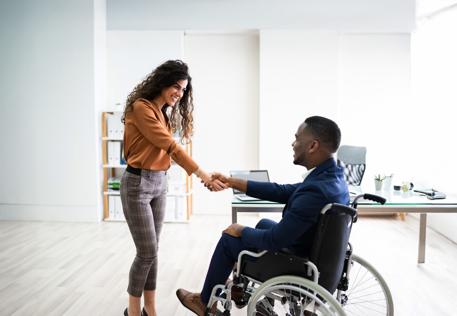 Woman shaking hands with a man in a wheelchair, office setting.