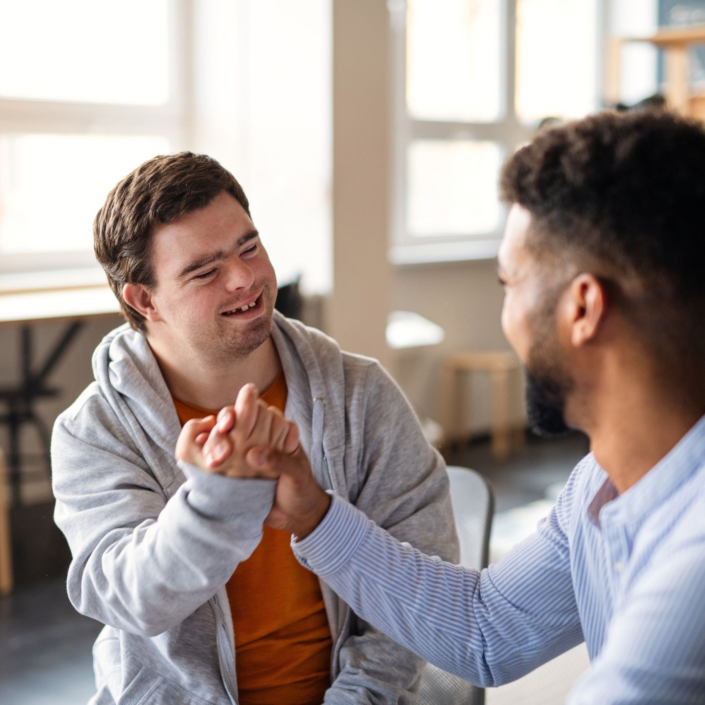 Man with Down syndrome smiles, high-fiving another man indoors.